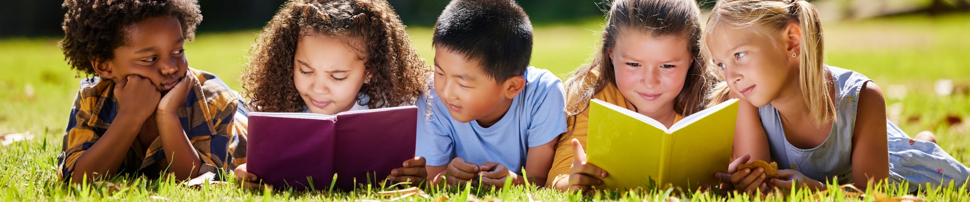 Five children laying on the grass, looking at books